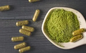 kratom powder in a bowl next to capsules