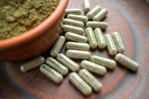 green capsules of kratom on table next to bowl of kratom