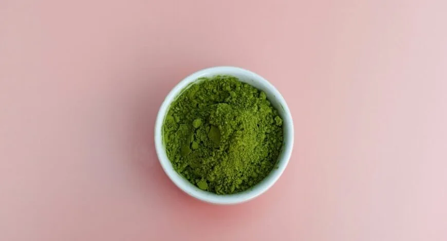 A bowl of green powder on a pink background