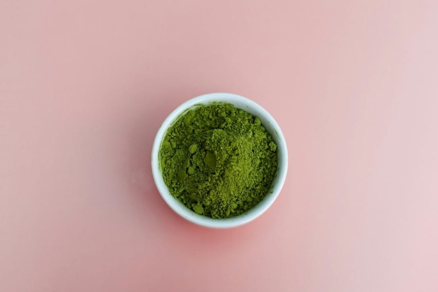 A bowl of green powder on a pink background